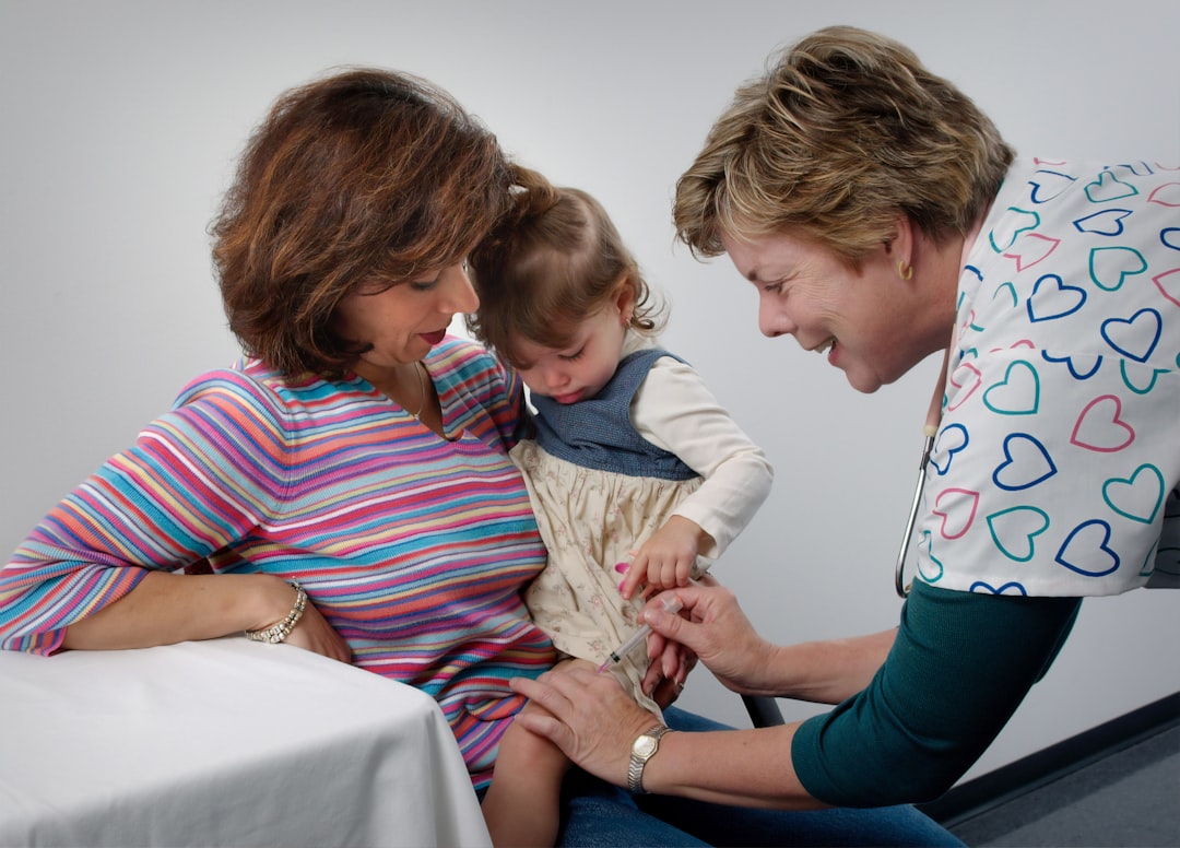 This photograph showed a young child being cradled by her mother, while she was receiving an intramuscular vaccination in her left thigh muscle. Notice that the nurse had immobilized the young girls leg using her left hand.